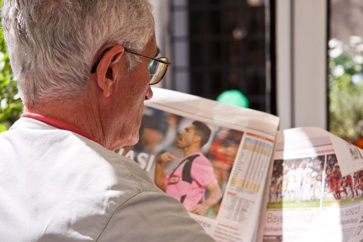 Old man with glass reading news